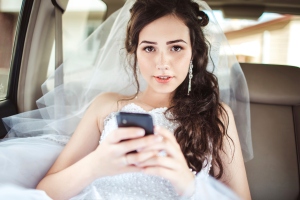 Beautiful bride sitting in car straight with mobile phone hairst
